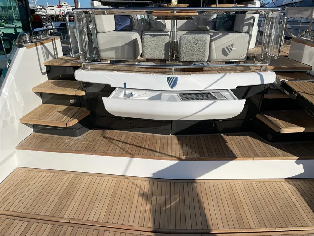 A luxury yacht's deck featuring wooden steps, a sleek white console, and plush seating in the background under bright sunlight.